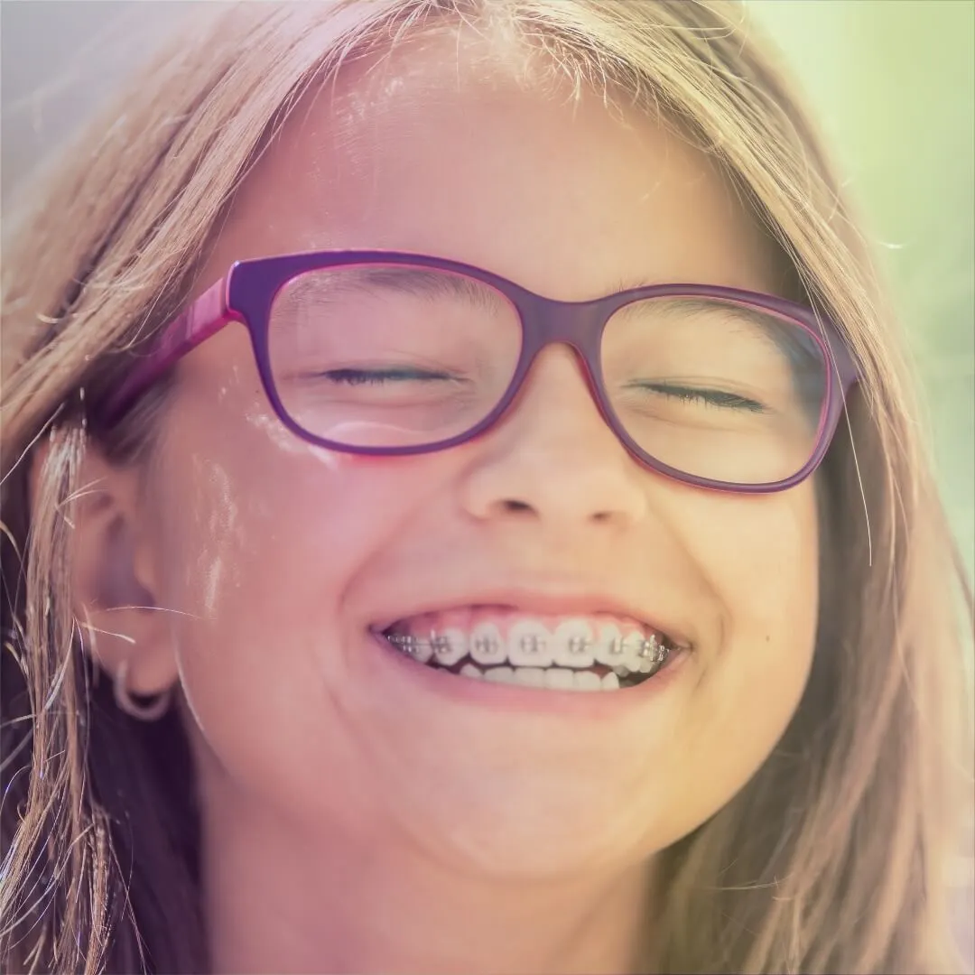 Ortodontista em Ouro Preto: adolescente, menina, sorrindo de aparelho fixo e óculos, com os olhos fechados.